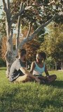 VERTICAL VIDEO, Happy smiling couple talking while sitting on the grass in the park. Backlight