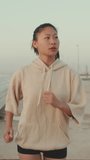 VERTICAL VIDEO, young athletic woman running along the promenade. Sportswoman in sportswear exercising outdoors at morning time