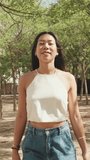 Vertical video, Beautiful brunette girl dressed in white top and jeans enjoys the weekend walking in the city park