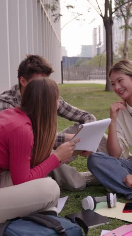 Group of young international university students sitting on the grass outside the faculty building. Friends gathered concentrated studying together with workbooks on campus
