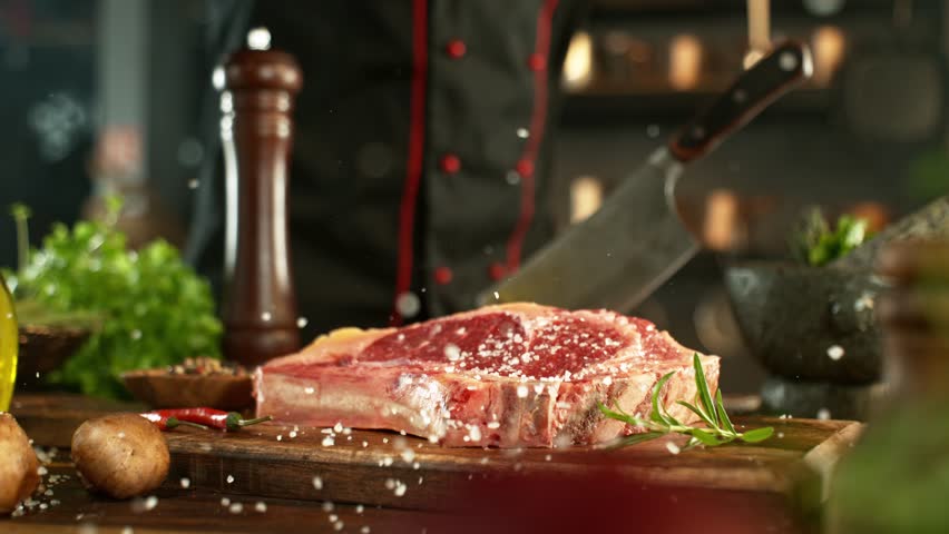 Close-up of falling salt on raw beef steak in kitchen, super slow motion, filmed on high speed cinematic camera at 1000 fps. Camera movement.