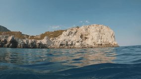 Coastal seascape with rocky shore from water level, slow motion. Mediterranean sea, Greece