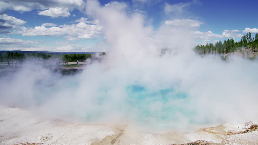 A hot spring in Yellowstone national park emits a dense cloud of steam, contrasting starkly with the deep blue sky and hinting at the potent geological forces at play. Slow Motion, 4K RAW. 
