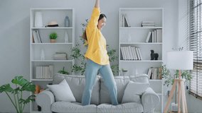 On the sofa in her living room, a young Asian woman dances. Asian woman with a smile relaxing at home, happy and in good mental and physical health, wearing headset and listening to music - Powered by Shutterstock - Get 15% off with code: PIKWIZARD15
