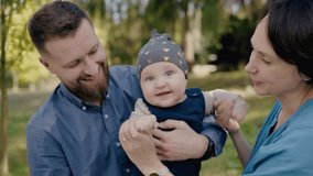 A couple is sharing a happy moment in the park, holding a baby under a tree. The man is wearing a hat and giving a thumbs up gesture while the woman smiles. - Powered by Shutterstock - Get 15% off with code: PIKWIZARD15