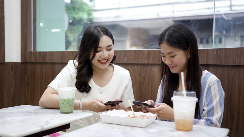 Two young asian women friends sitting at coffee shop having a coffee and chatting with smiling laugh and happiness moment. Female friends meeting at cafe on a weekend, positive attitude relationship