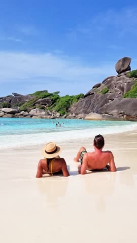 A couple is relaxing on a beach, gazing at the beautiful ocean under the clear sky. The tranquil natural landscape brings peace and leisure to their travel experience Similan Islands, Thailand Royalty-Free Stock Footage #3455933231