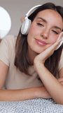 Happy young woman relaxing at home listening to music with wireless headphones. Leisure and domestic lifestyle. Vertical screen HD video.