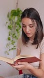 Young beautiful girl reading a book on the bed. Leisure activities and domestic lifestyle concept. Vertical screen HD video.