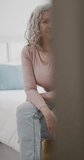 Vertical video portrait of senior caucasian woman looking at camera and sitting on bed, slow motion. Retirement, domestic life, lifestyle and cooking.