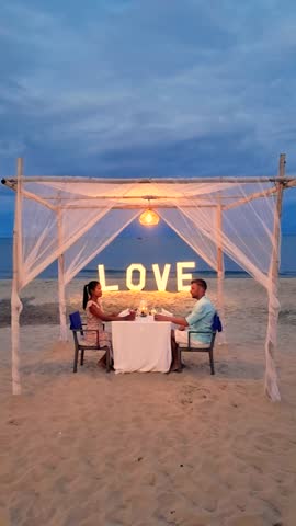 A couple is seated at a beach table under a canopy, enjoying the shade and leisure time while taking in the picturesque landscape and horizon romantic, Valentine dinner, Hua Hin ,Thailand
