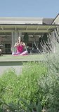 Vertical video of relaxed biracial couple practicing yoga in garden. Free time, activity and relax.