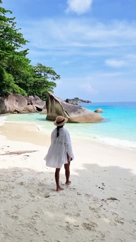 A woman stands on the beach, gazing out at the vast expanse of water, under a sky dotted with clouds. The tranquil landscape invites thoughts of leisure and travel Similan Islands, Thailand Royalty-Free Stock Footage #3455997321