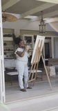 Vertical video of happy senior african american woman painting in slow motion. Spending quality time at home, retirement and art.