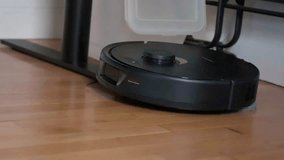 Slow-motion footage captures an autonomous robot cleaning, stuck on a table's leg, as it continues cleaning a hardwood floor.