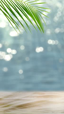 fresh green palm leaf and white sand on blurred glittering bokeh light water background, beautiful idyllic sand beach backdrop with product display for summer vacation, travel and relaxation outdoors