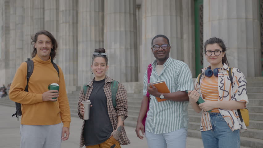 Young happy male and female students standing together outdoors in front of university, posing at camera and smiling. Group portrait