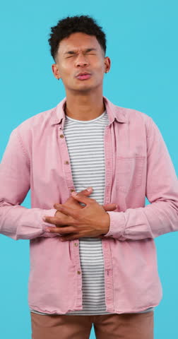 Stomach ache, pain or indigestion and face of man on blue background in studio with abdominal nausea. Healthcare, medical or belly problems and a young person on a vertical backdrop with tummy cramps Royalty-Free Stock Footage #3456037387
