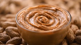 Peanut butter in a glass bowl, rotation over raw peanuts background. Creamy smooth peanut butter in jar backdrop. Mixed with a spoon, organic food. American cuisine. Slow motion - Powered by Shutterstock - Get 15% off with code: PIKWIZARD15