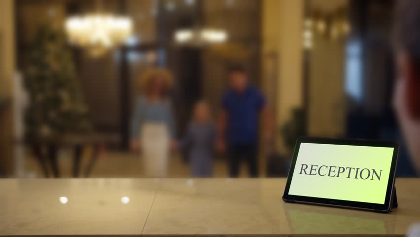 A family on holiday in a hotel approaches to the reception desk with a tablet labeled reception