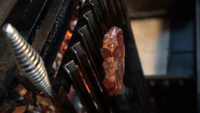 A juicy beef steak is grilled over fiery coals on an iron grill on a dark background in a flame of smoke. barbecue, chef frying meat on the grill. We cook dinner over a hot fire. vertical video