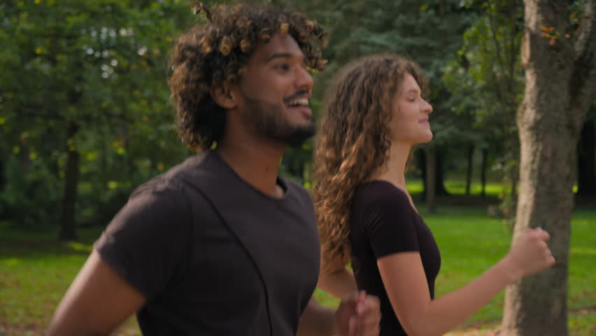 Multiracial love couple runners workout running jogging in city park happy gen z girlfriend boyfriend sport people run together healthy Caucasian woman Indian man pointing on way direction jog outside