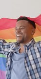 Vertical video of happy african american man holding lgbt rainbow flag, slow motion. Pride, love and tolerance.