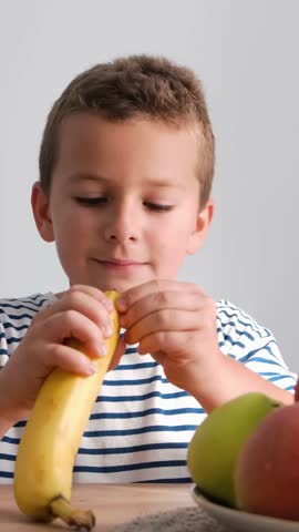 Boy peels banana near bowl of apples, satisfying food craving with natural foods