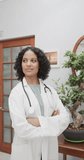 Vertical video of portrait of biracial female doctor crossing arms and smiling, slow motion. Medical staff, medicine and healthcare.