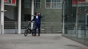 In this 4K video, we highlight the seamless integration of technology and environmental awareness. Witness the businessman with helmet and backpack, utilizing his phone while walking with his electric
