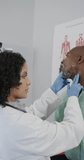 Vertical video of diverse female doctor examining male patient in consulting room, slow motion. Medical staff, medicine and healthcare.