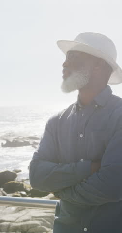 Vertical video of portrait of senior african american man on promenade by the sea, slow motion. Spending quality time, lifestyle, vacation and retirement concept.
