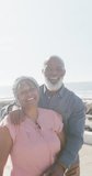 Vertical video of senior biracial couple embracing on promenade by the sea, slow motion. Spending quality time, lifestyle, vacation and retirement concept.
