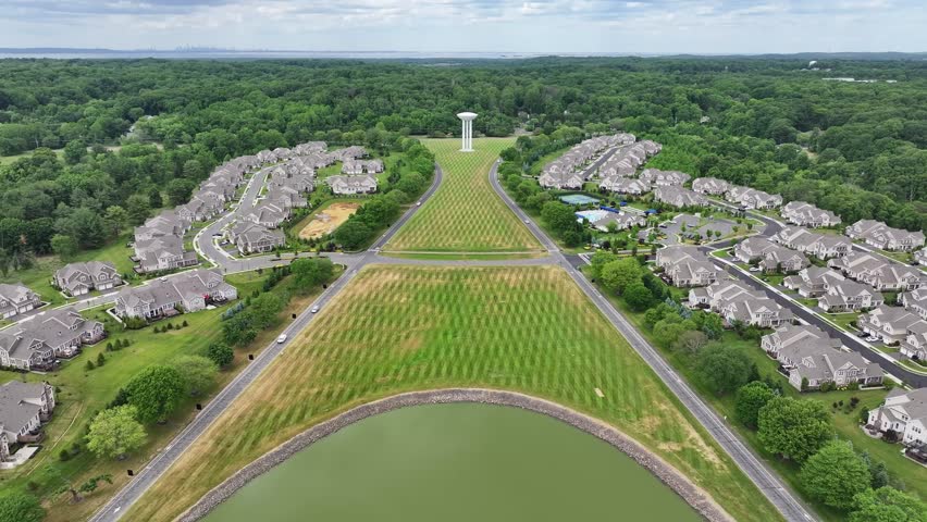 A view of a residential area with a large green pond in the middle. The houses are spread out and there are several trees in the background