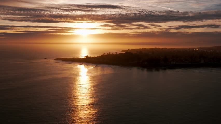 Panning shot of a drone aerial over a peninsula in Santa Cruz at sunset with surfers
