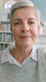 Mature woman, waving and video call talk in house library, home living room or interior with people. Face portrait, smile or happy person in communication, greeting gesture and social media zoom chat