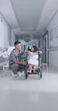 Vertical video of asian male surgeon high fiving with girl in hospital in slow motion. Medicine, health and care.