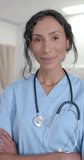 Vertical video of portrait of happy biracial female doctor looking at camera, in slow motion. Hospital, medicine and healthcare.
