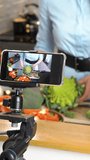 Beautiful young woman streaming broadcast video blog about tasty and healthy food at the home kitchen using her smartphone