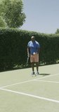 Vertical video of happy senior african american man playing tennis at tennis court. Spending quality time, sport, retirement.