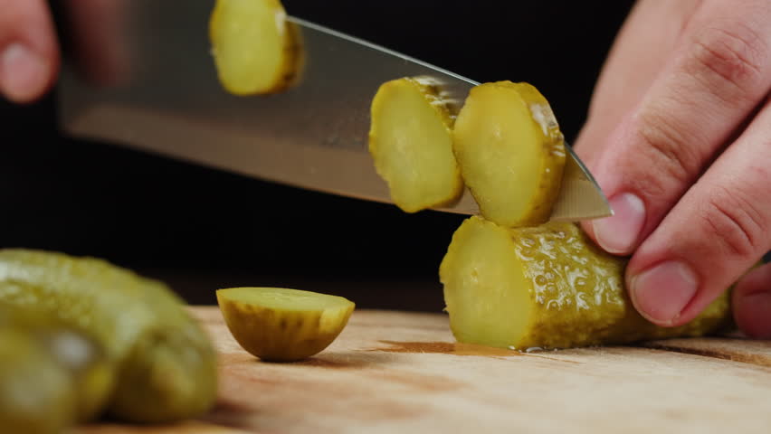 Chef slicing Salted pickles with knife from jar can, Cucumbers preservations, conservation. Salted, Hungarian pickled cucumbers in a jar on an old wooden table in the garden with herbs, dill, garlic