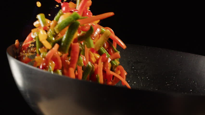 Chef cooking flambe vegetables mix on wok frying pan close-up. Color hot and sweet peppers on fire throwing them on pan. Restaurant Food concept
