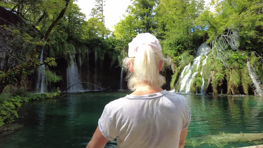 Woman by the lake of Galovacki Buk waterfall of Plitvice National Park in Croatia. Natural forest park with lakes and falls in the Lika region. UNESCO World Heritage of Croatia named Plitvicka Jezera