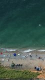Aerial timelapse view over sandy beach during summer sunset. Crowds of happy people relax by the blue water of the sea bay. Holiday recreation in a natural ocean setting. Vertical video