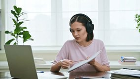 Young female college student in headphones studying using laptop computer for video chat