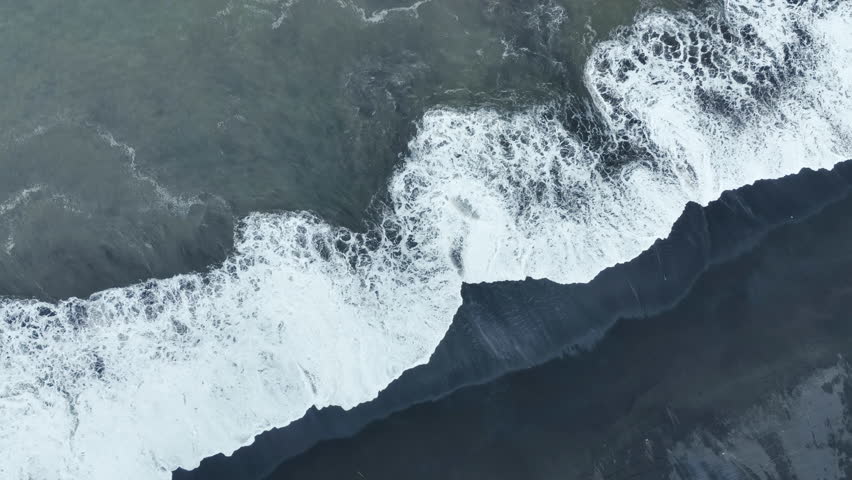 Drone aerial view of black sand beach with ocean and waves in Bali, Indonesia.