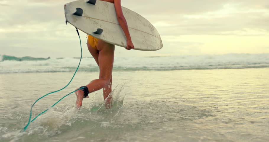 Woman, surfer and running with water splash on beach for waves, sport or outdoor surfing in nature. Rear view of female person on ocean coast or sea for surfing, holiday or weekend with surfboard