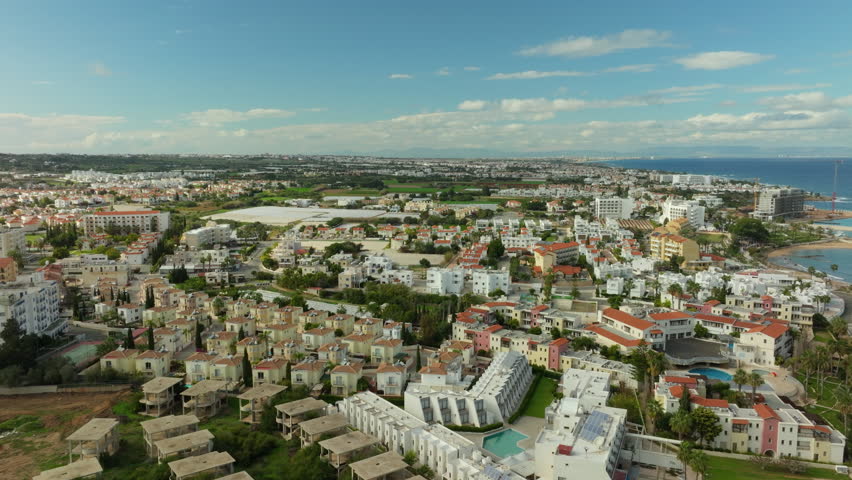 Panoramic aerial view of Pernera, Cyprus, showcasing the dense residential area, tourist accommodations, and the vast Mediterranean Sea in the backdrop.