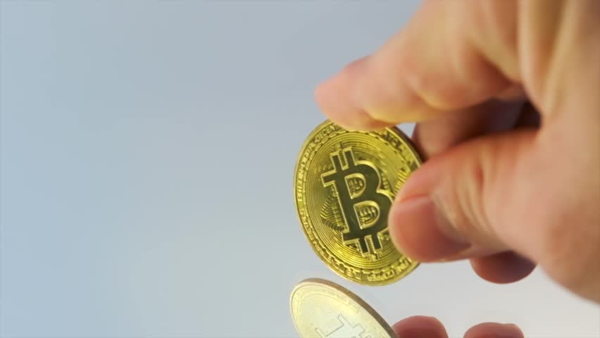Demonstration of bitcoin coin, gold cryptocurrency, in fingers of man, against the background of mirror of light surface, close up. Digital wealth. Online trading concept. Copy space. Royalty-Free Stock Footage #3456653715
