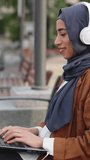 Muslim woman turning to smile to the camera while working on a laptop outdoors